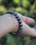 Hand wearing a black beaded bracelet with a blurred green background